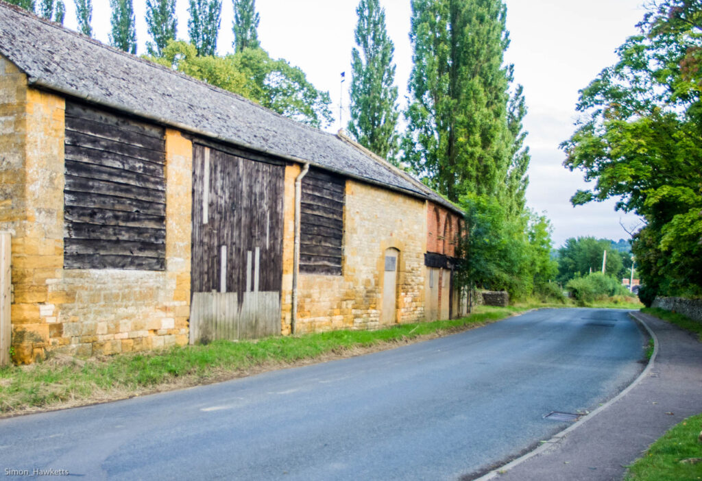 A cotswold stone barn by a road in Gloucestershire