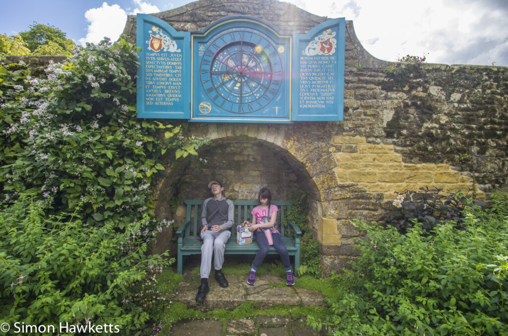 two children sitting on a seat under an astronomical clock at snowshill manor